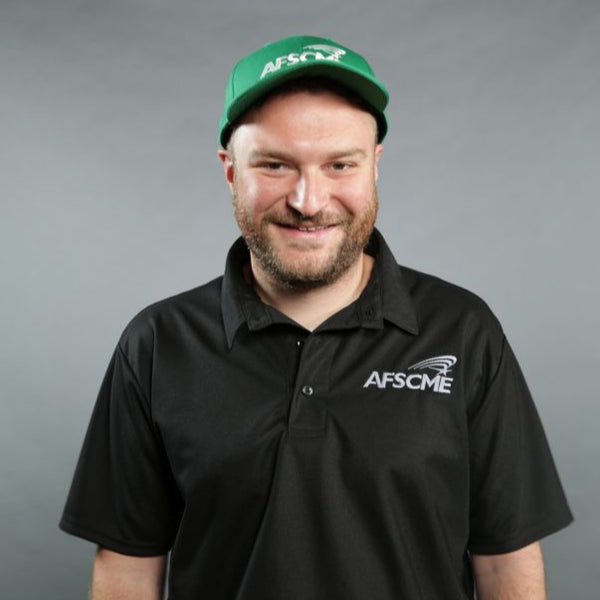 Man wearing a black AFSCME shirt and green cap on a gray background